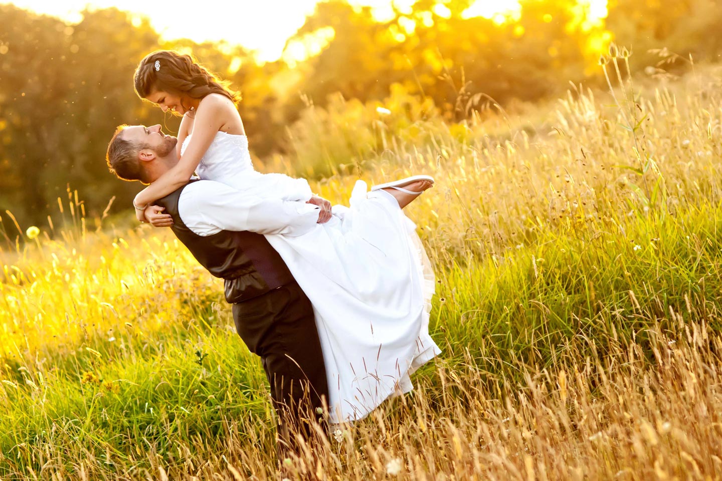 groom pics up bride in a field
