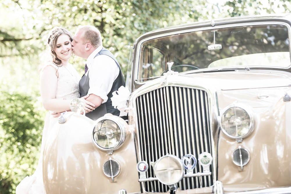 groom kissing bride by old car